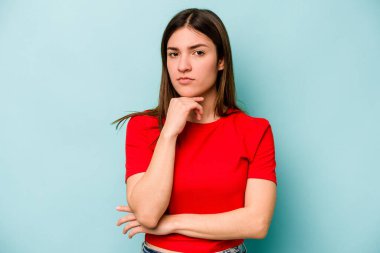 Kafkasyalı genç bir kadın mavi arka planda izole edilmiş şüpheli, belirsiz, seni muayene ediyor..