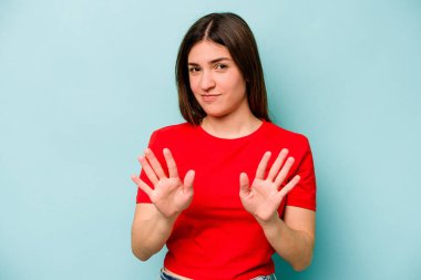 Mavi arka planda izole edilmiş genç beyaz kadın tiksinti belirtisi gösteren birini reddediyor..