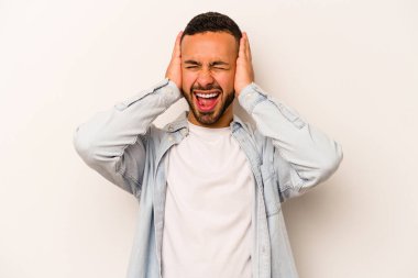 Latin kökenli genç adam beyaz arka planda izole edilmiş. Kulakları kulaklarıyla kapatıyor. Çok fazla ses duymamaya çalışıyor..