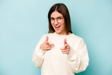 Mavi arka planda izole edilmiş genç beyaz kadın parmaklarıyla ön tarafı işaret ediyor..