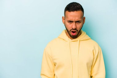 Genç İspanyol adam mavi arka planda izole edilmiş çok kızgın, öfkeli, hayal kırıklığına uğramış bağırıyor..