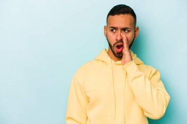 Mavi arka planda izole edilmiş genç İspanyol bir adam gizli bir sıcak fren haberi veriyor ve yana bakıyor.