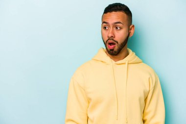 Genç İspanyol bir adam mavi arka planda izole edilmiş. Gördüğü bir şey yüzünden şok oluyor..