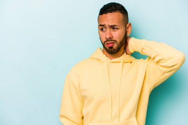 Genç İspanyol bir adam mavi arka planda izole edilmiş kafasının arkasına dokunuyor, düşünüyor ve bir seçim yapıyor..