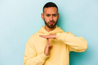 Mavi arka planda izole edilmiş genç İspanyol bir adam bir mola hareketi gösteriyor..