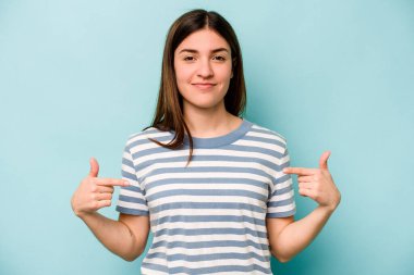 Mavi arka planda izole edilmiş genç beyaz bir kadın gömlek fotokopisini elle gösteriyor, gururlu ve kendinden emin.