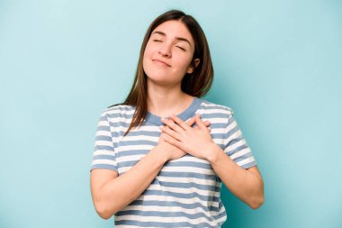 Mavi arka planda izole edilmiş beyaz bir kadın, dost canlısı bir ifadeye sahip, avuçlarını göğsüne bastırıyor. Aşk konsepti.
