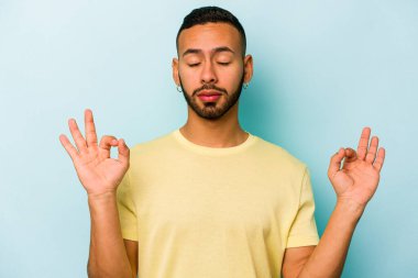 Mavi arka planda izole olmuş genç İspanyol adam sıkı çalışma gününden sonra rahatlıyor, yoga yapıyor..