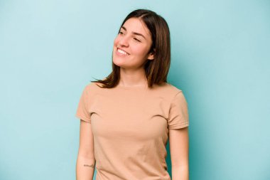 Genç beyaz kadın mavi arka planda izole edilmiş rahat ve mutlu bir şekilde gülüyor, boynunda dişlerini gösteriyor..