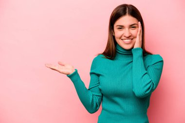 Pembe arka planda izole edilmiş genç beyaz kadın avuç içinde fotokopi alanı tutuyor, el üstünde tutuyor. Şaşırmış ve mutlu..