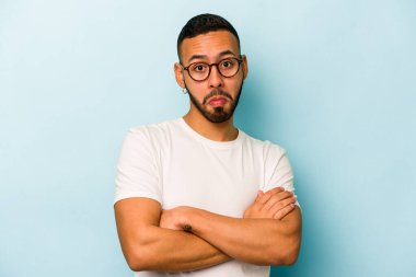 Mavi arka planda izole edilmiş genç bir İspanyol omuz silker ve gözleri açık kalır..