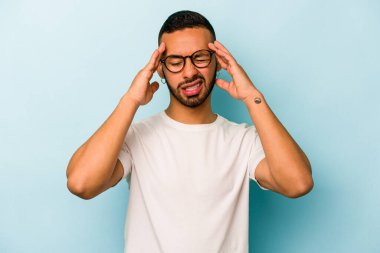 Genç İspanyol adam mavi arka planda izole edilmiş tapınaklara dokunuyor ve baş ağrısı çekiyor..