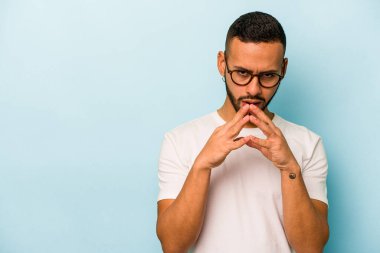 Latin kökenli genç bir adam mavi arka planda izole edildi. Aklında bir plan kuruyor, bir fikir kuruyor..