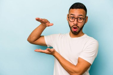 Mavi arka planda izole edilmiş genç İspanyol adam elleri arasında bir kopya alanı tutarken şok oldu ve hayrete düştü..