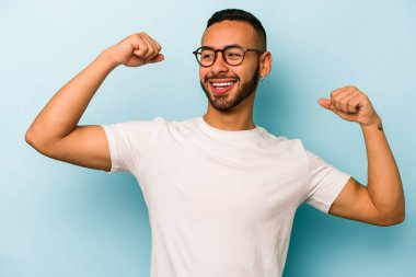 Mavi arka planda izole edilmiş genç İspanyol bir adam zaferden sonra yumruk kaldırıyor, kazanan konsept..