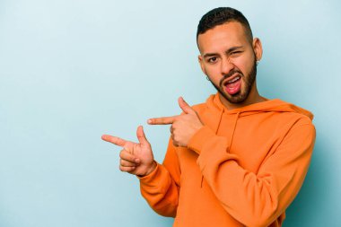 Mavi arka planda izole edilmiş genç İspanyol adam işaret parmaklarıyla fotokopi alanını işaret ederek heyecan ve arzuyu ifade ediyor..