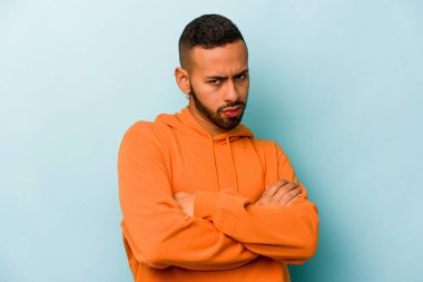 Mavi arka planda izole edilmiş, hoşnutsuzca kaşlarını çatmış, kollarını kavuşturmuş genç bir İspanyol..