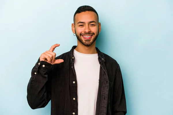 Joven Hombre Hispano Aislado Sobre Fondo Azul Sosteniendo Algo Poco — Foto de Stock