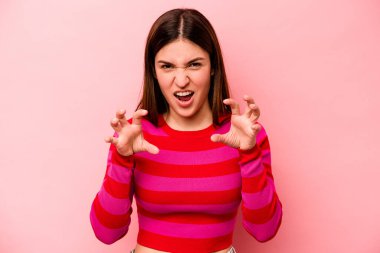 Pembe arka planda izole edilmiş genç beyaz kadın pençelerini kedi taklidi yaparken gösteriyor, agresif bir hareket..