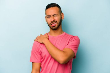 Mavi arka planda izole edilmiş genç İspanyol bir adam omuz ağrısı çekiyor..