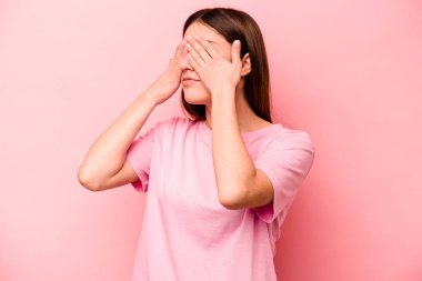 Pembe arka planda izole edilmiş genç beyaz kadın elleriyle gözlerini kapatmaktan korkuyor..
