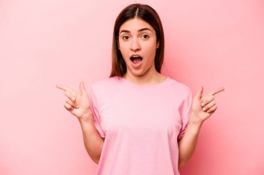 Pembe arka planda izole edilmiş genç beyaz kadın farklı kopya alanlarını gösteriyor, birini seçiyor, parmağıyla gösteriyor..
