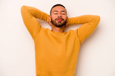 Beyaz arka planda izole edilmiş genç İspanyol bir adam kendini güvende hissediyor, elleri başının arkasında..