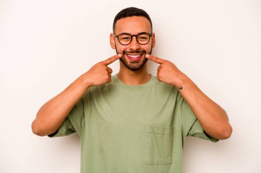 Beyaz arka planda izole edilmiş genç İspanyol adam gülümsüyor, parmaklarını ağıza doğrultuyor..