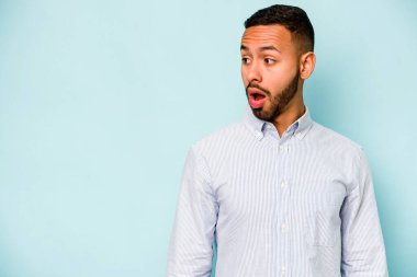 Genç İspanyol bir adam mavi arka planda izole edilmiş. Gördüğü bir şey yüzünden şok oluyor..