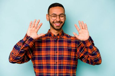 Mavi arka planda izole edilmiş genç İspanyol adam on numarayı elleriyle gösteriyor..