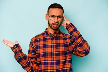 Genç İspanyol bir adam mavi arka planda izole edilmiş ve elinde bir ürün tutuyor..