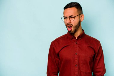 Genç İspanyol adam mavi arka planda izole edilmiş çok kızgın, öfkeli, hayal kırıklığına uğramış bağırıyor..