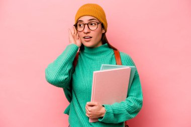 Pembe arka planda izole edilmiş genç beyaz kadın bir dedikoduyu dinlemeye çalışıyor..