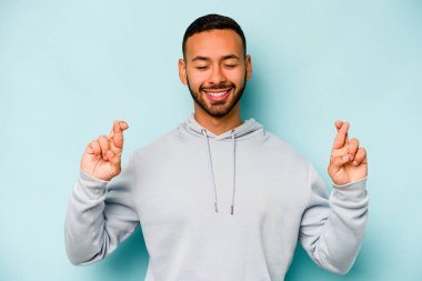 Genç İspanyol adam mavi arka planda izole edilmiş şans dilemek için şans diliyor.