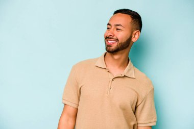 Mavi arka planda izole edilmiş genç bir İspanyol. Rahatlamış ve mutlu bir şekilde gülüyor. Boynunda dişler var..