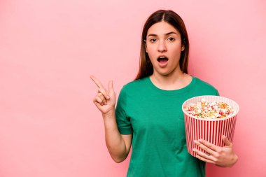 Elinde patlamış mısır tutan beyaz bir kadın. Pembe arka planda izole edilmiş. Yan tarafı işaret ediyor.