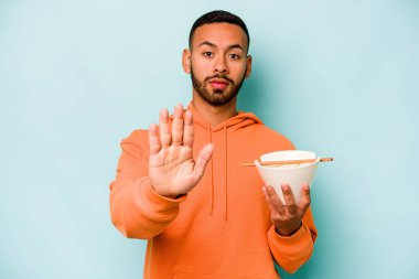 Mavi arka planda izole edilmiş erişte yiyen genç İspanyol kadın elini uzatıp dur işaretini göstererek seni engelliyor..