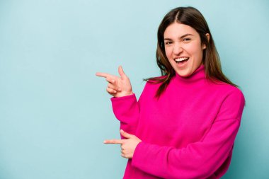 Mavi arka planda izole edilmiş genç beyaz kadın işaret parmaklarıyla fotokopi alanını işaret ederek heyecan ve arzusunu ifade ediyor..