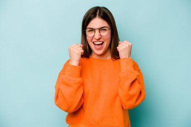 Genç beyaz kadın mavi arka planda izole edilmiş tasasız ve heyecanlı bir şekilde tezahürat yapıyor. Zafer konsepti.