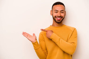 Beyaz arka planda izole edilmiş genç İspanyol bir adam heyecanlı bir şekilde avuç içinin bir kopyasını tutuyor..