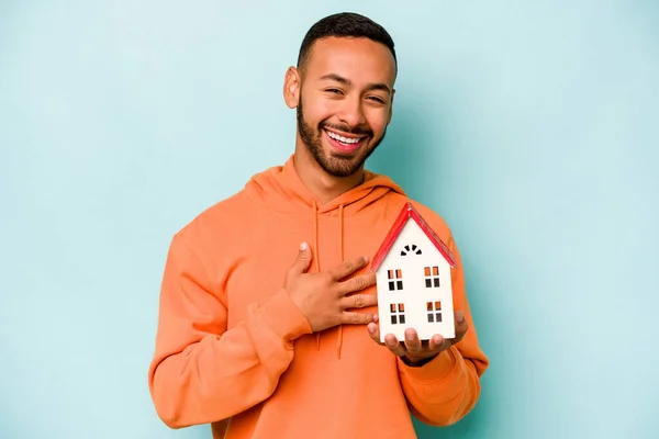 Young Hispanic Man Holding Toy House Isolated Blue Background Laughs — Stock Photo, Image