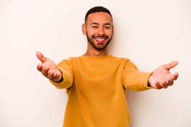 Beyaz arka planda izole edilmiş genç bir İspanyol hoş geldin ifadesi sergiliyor..