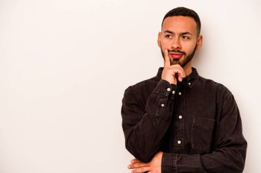 Beyaz arka planda izole edilmiş genç bir İspanyol şüpheli ve şüpheci bir ifadeyle yana bakıyor..