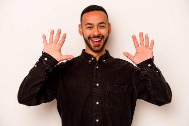 Latin kökenli genç bir adam beyaz arka planda izole edilmiş. Hoş bir sürprizle karşılaşıyor, heyecanlı ve el kaldırıyor..