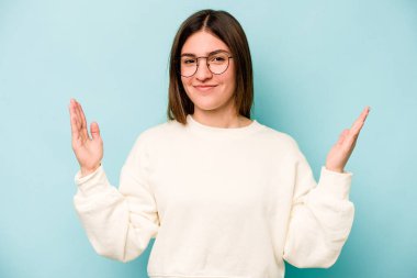 Kafkasyalı genç bir kadın mavi arka planda izole edilmiş. Elinde parmakları olan, gülümseyen ve kendinden emin bir şey var..