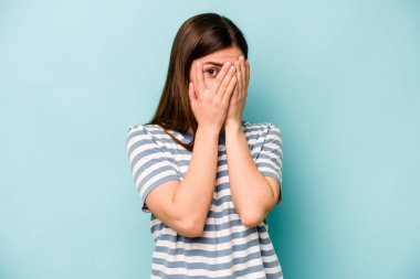 Mavi arka planda izole edilmiş genç beyaz kadın parmaklarıyla gözünü kırp korkmuş ve gergin..
