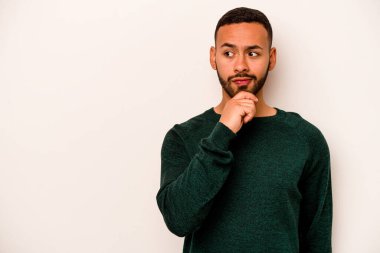 Beyaz arka planda izole edilmiş genç bir İspanyol şüpheli ve şüpheci bir ifadeyle yana bakıyor..