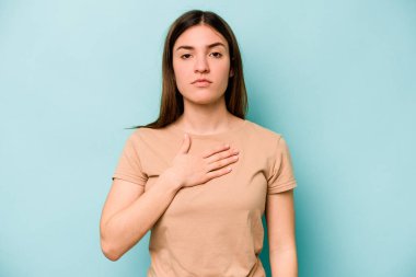 Beyaz bir kadın mavi arka planda izole edilmiş yemin ediyor, elini göğsüne koyuyor..
