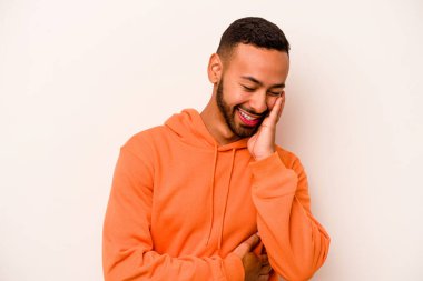 Beyaz arka planda izole edilmiş genç İspanyol adam mutlu bir şekilde gülüyor ve ellerini karnının üstünde tutarak eğleniyor..