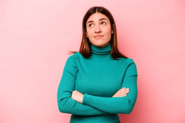 Pembe arka planda izole edilmiş genç beyaz kadın hedeflere ve amaçlara ulaşma hayali kuruyor.